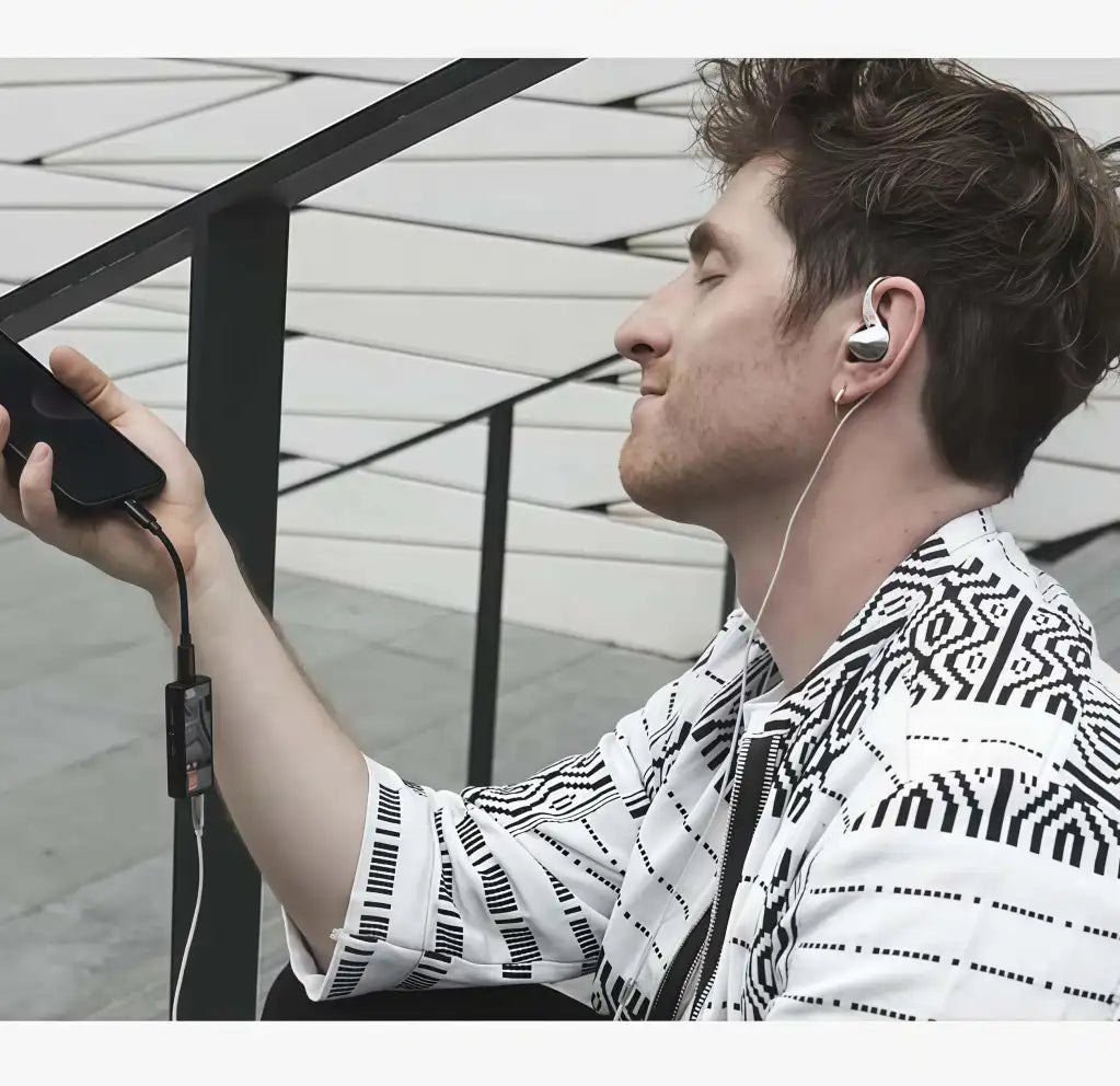 Man enjoying music with earphones using Questyle M15C portable DAC connected to smartphone.